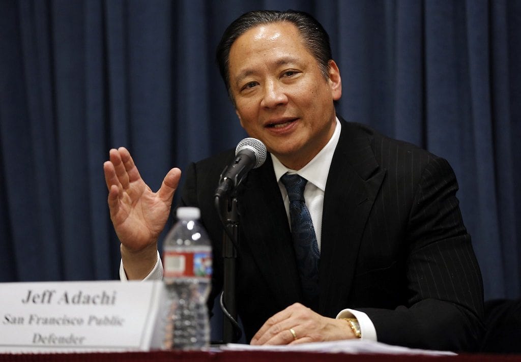 Jeff Adachi in a white shirt and black suit speaking in front of a microphone.